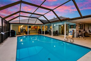 An indoor swimming pool with a glass ceiling, surrounded by a covered patio area with seating and a dartboard.