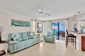 A living room with a sofa, armchair, and a dining area with a kitchen counter.