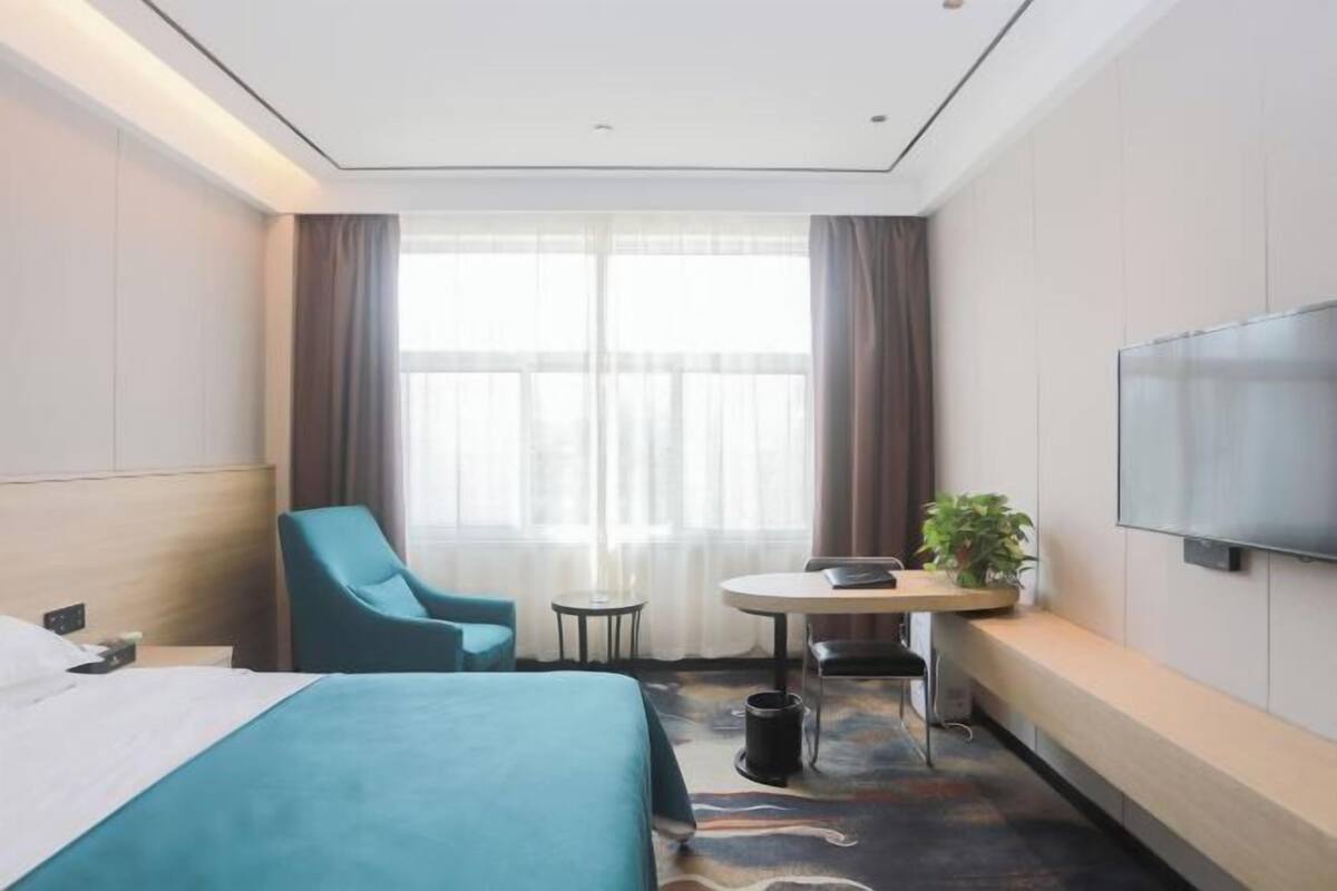 Habitación de hotel con cama, escritorio, silla, televisor y ventana con cortinas.