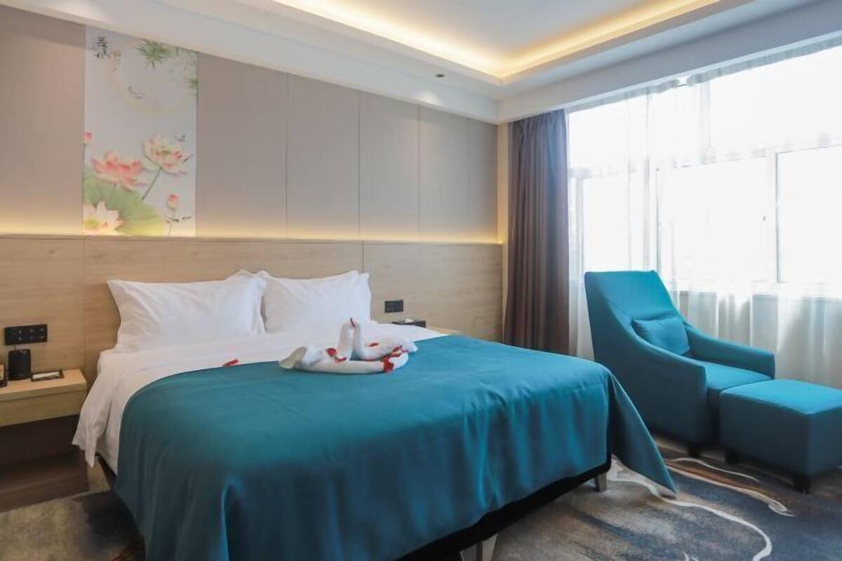 Una habitación de hotel con una cama grande, un sillón azul y una pared con un cuadro floral.