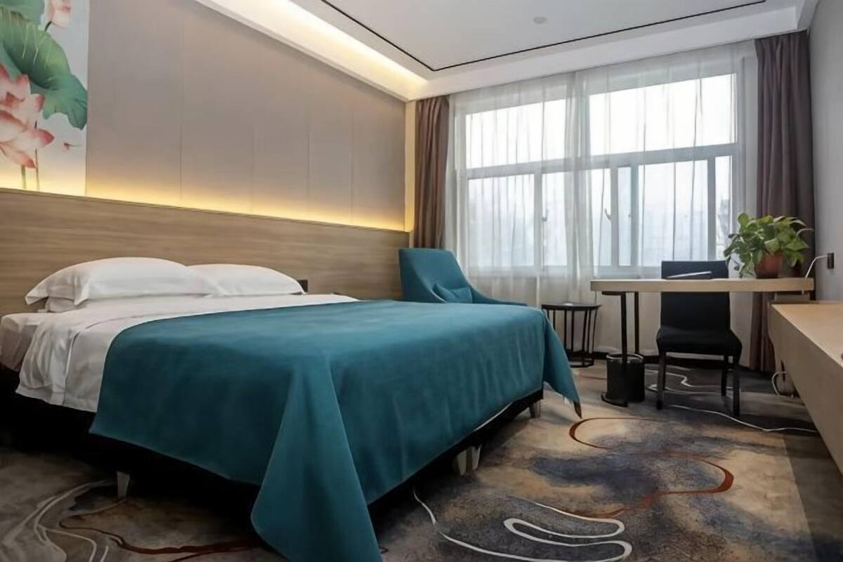 Habitación de hotel con cama, escritorio, silla y ventanas amplias.