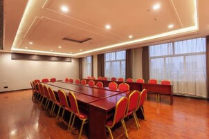 Un salón de conferencias con una larga mesa y sillas rojas, ventanas amplias y suelo de madera.
