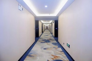 Un pasillo de hotel con alfombra estampada, iluminación empotrada y un largo recorrido hacia la recepción.