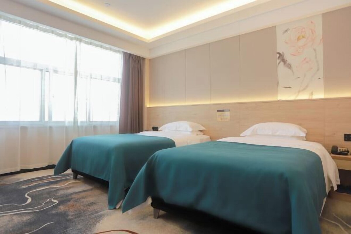 Habitación de hotel con dos camas, un ventanal grande y un cuadro floral en la pared.