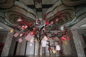 Une sculpture en forme d’arbre ornée de notes suspendues, placée dans un hall d’entrée.