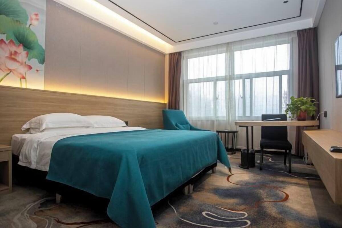 Habitación de hotel con cama, escritorio, silla y un ventanal con cortinas.
