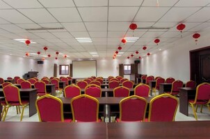 Un salón de conferencias con varias mesas y sillas, una pantalla de proyector y faroles rojos en el techo.