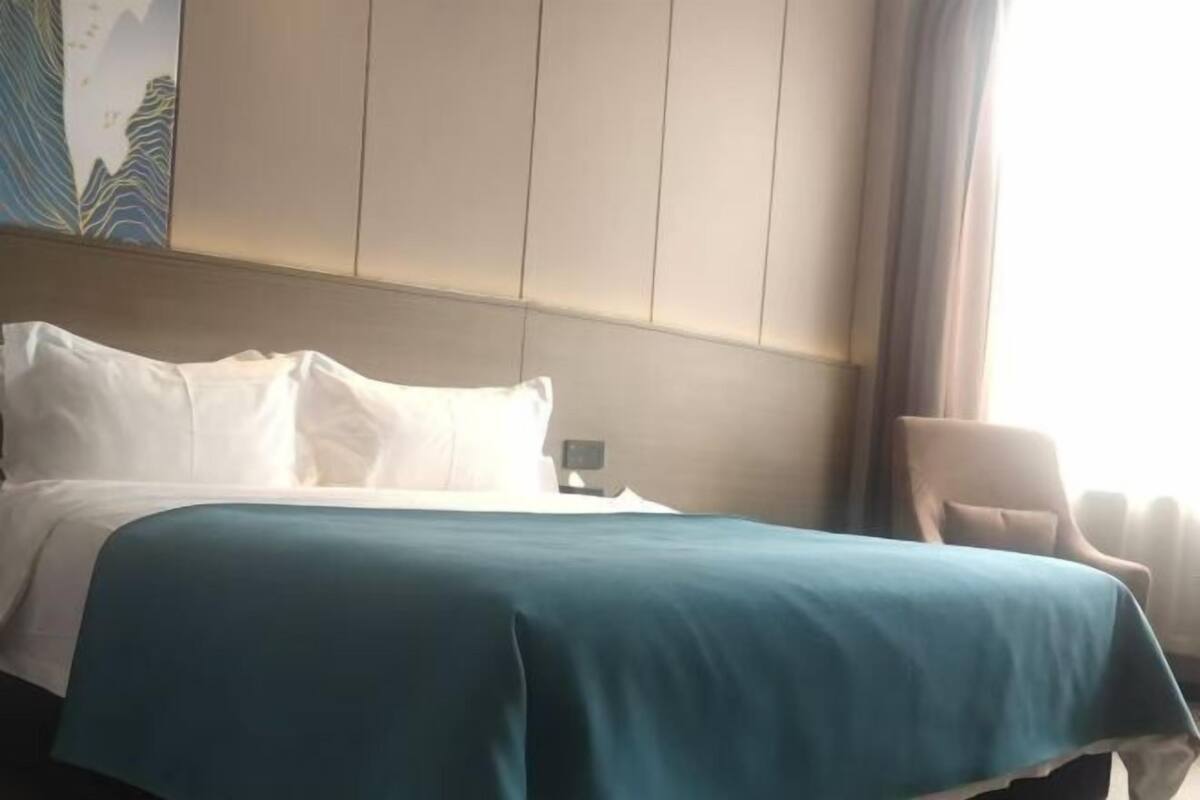 Una habitación de hotel con cama, mesita de noche, una silla y un cuadro en la pared.