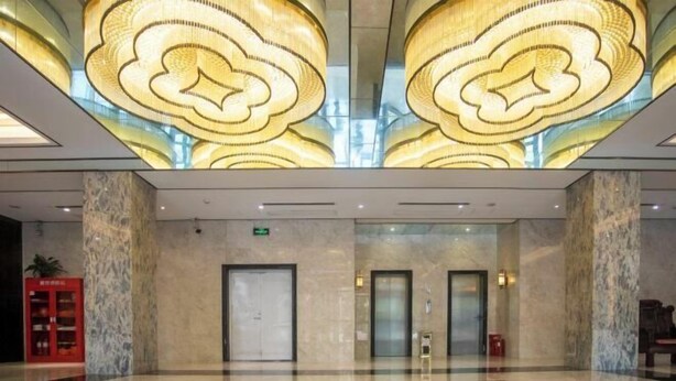 Un hall d’entrée spacieux, doté d’un sol à motifs géométriques, de grands luminaires décoratifs au plafond et de colonnes en marbre.