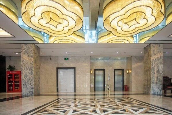 A spacious lobby with a geometric patterned floor, two elevators, and a ceiling with a large, circular light fixture.