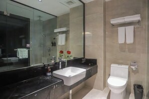 Une salle de bain moderne avec un grand miroir, un lavabo blanc, des toilettes et une douche à parois de verre.