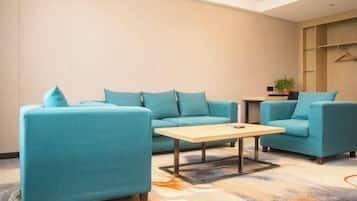 Ein modernes Hotelzimmer mit aquamarinfarbenen Sofas, einem Holztisch und einem gemusterten Teppich.