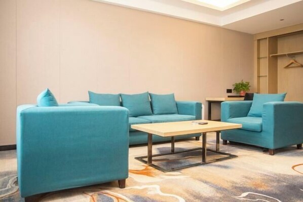Une chambre d’hôtel moderne avec des canapés de couleur turquoise, une table basse en bois et un tapis à motifs.