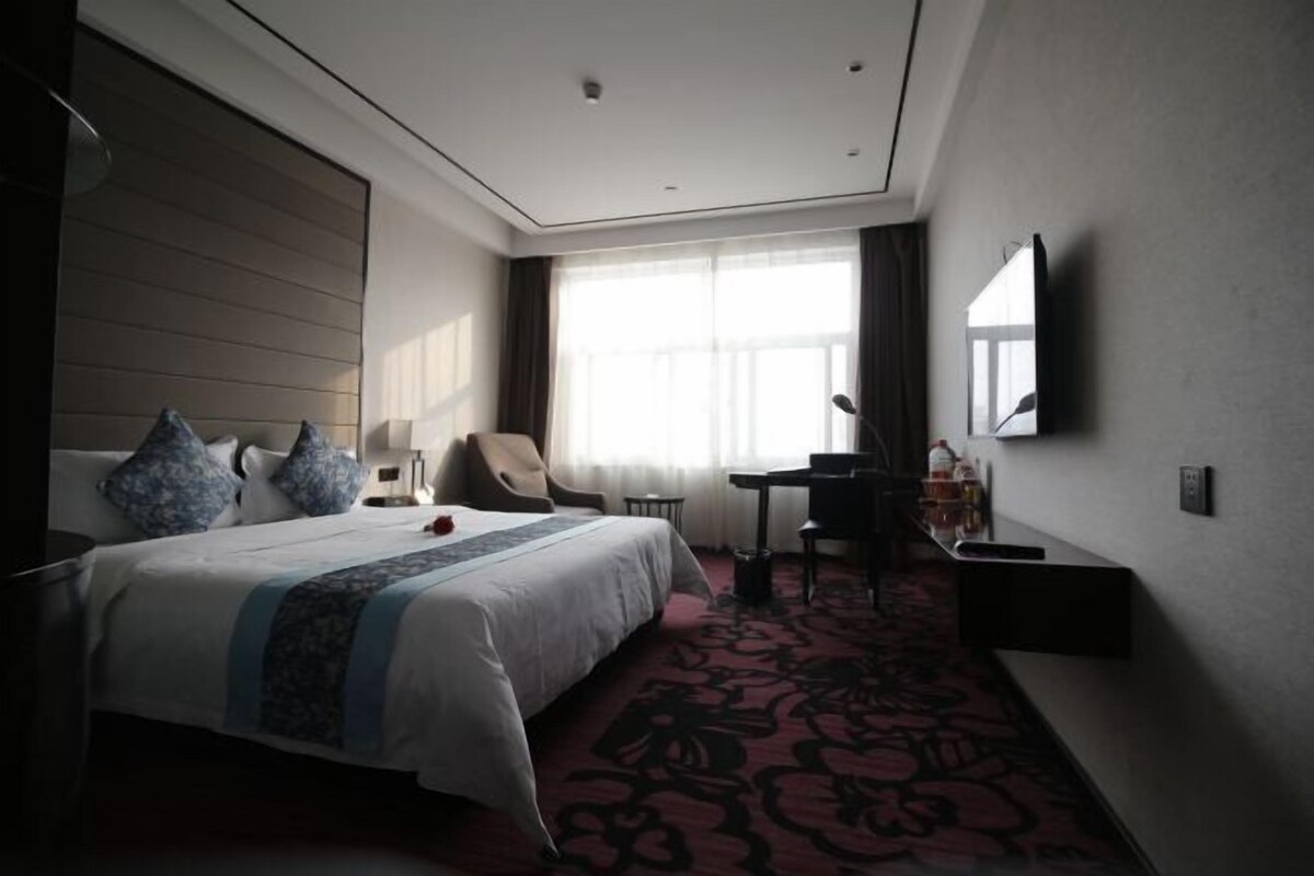 Une chambre d’hôtel avec un grand lit, un bureau, une chaise, une télévision et une fenêtre avec des rideaux.