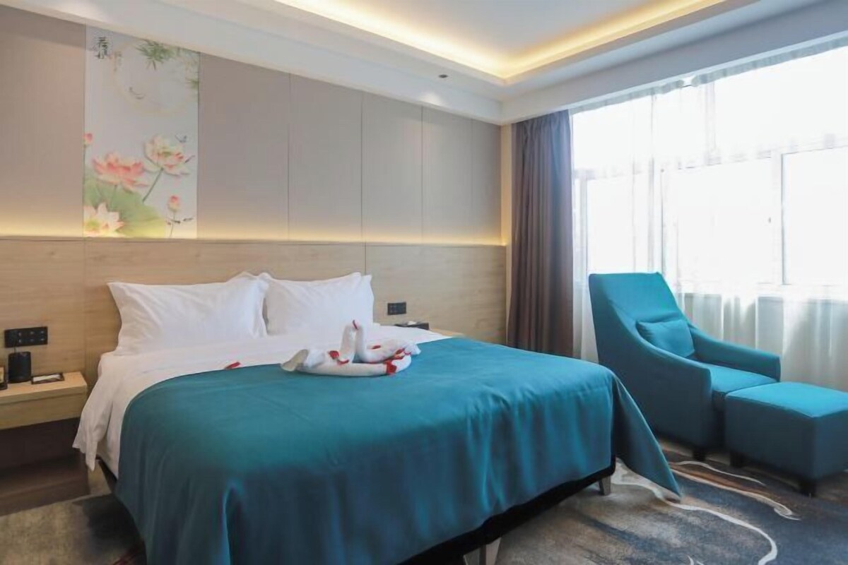 Une chambre d’hôtel avec un lit, un fauteuil bleu, une table de chevet et une grande fenêtre.