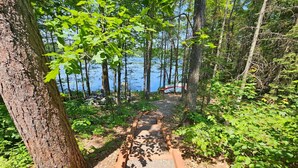 A forested path leading to a lake with a boat dock visible in the background. - Private lakefront escape for unforgettable group getaways (Cable)