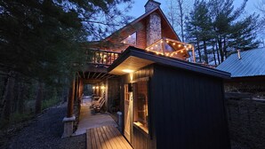 A log cabin with a porch, a stone chimney, and string lights. - Private lakefront escape for unforgettable group getaways (Cable)