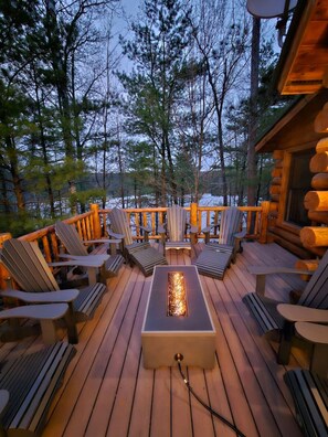A deck with Adirondack chairs, a fire pit, and a view of a forested area.