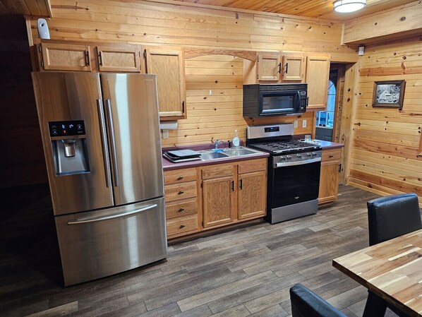 A compact kitchen with wooden cabinetry, stainless steel appliances, and a dining area with a table and chairs.