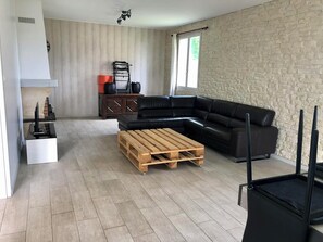 A living room with a black leather sofa, a wooden coffee table, a TV stand, and a stone wall.