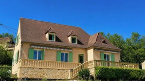 Ein zweistöckiges Haus mit Steinfassade, grünen Fensterläden und einem Ziegeldach.