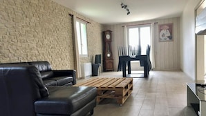 Ein Wohnzimmer mit Backsteinwand, einer schwarzen Ledersofa, einem Holztisch, einem Esstisch mit Stühlen, einer Uhr und einem Gemälde an der Wand.