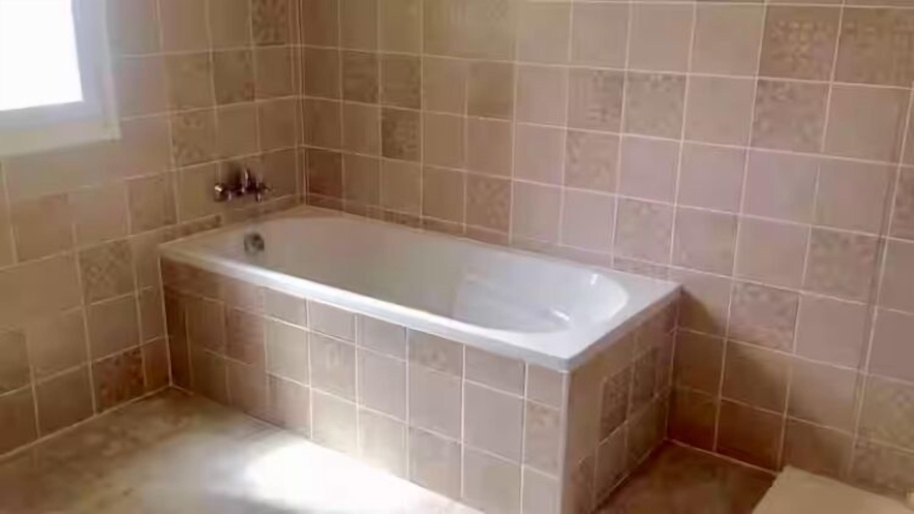 Un bagno con vasca, pareti piastrellate e una finestra.