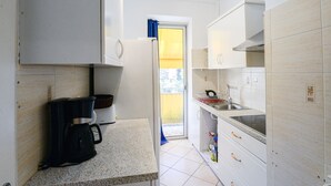 Una cocina compacta con muebles blancos, cafetera y pileta.
