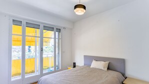 Un dormitorio con cama, mesita de noche, lámpara y ventana con persianas.