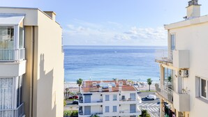 Un edificio frente al mar con balcones, cielo despejado y una playa al fondo.