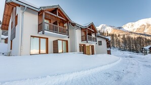 En toetages chalet med træbalkoner, store vinduer og en snebelagt indkørsel.