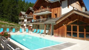 En træchalet med swimmingpool, balkoner og udsigt til skoven.