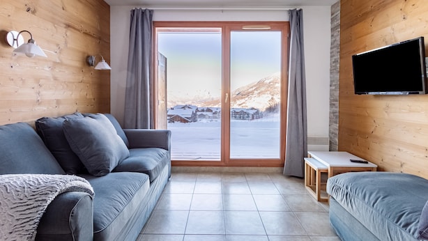 Et moderne værelse med træindretning, en grå sofa, et lille bord og et TV ophængt på væggen.