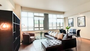 A modern living room with a sofa, armchairs, a glass coffee table, and a dining area with chairs. - 1-bed Apartment in City of London (London)
