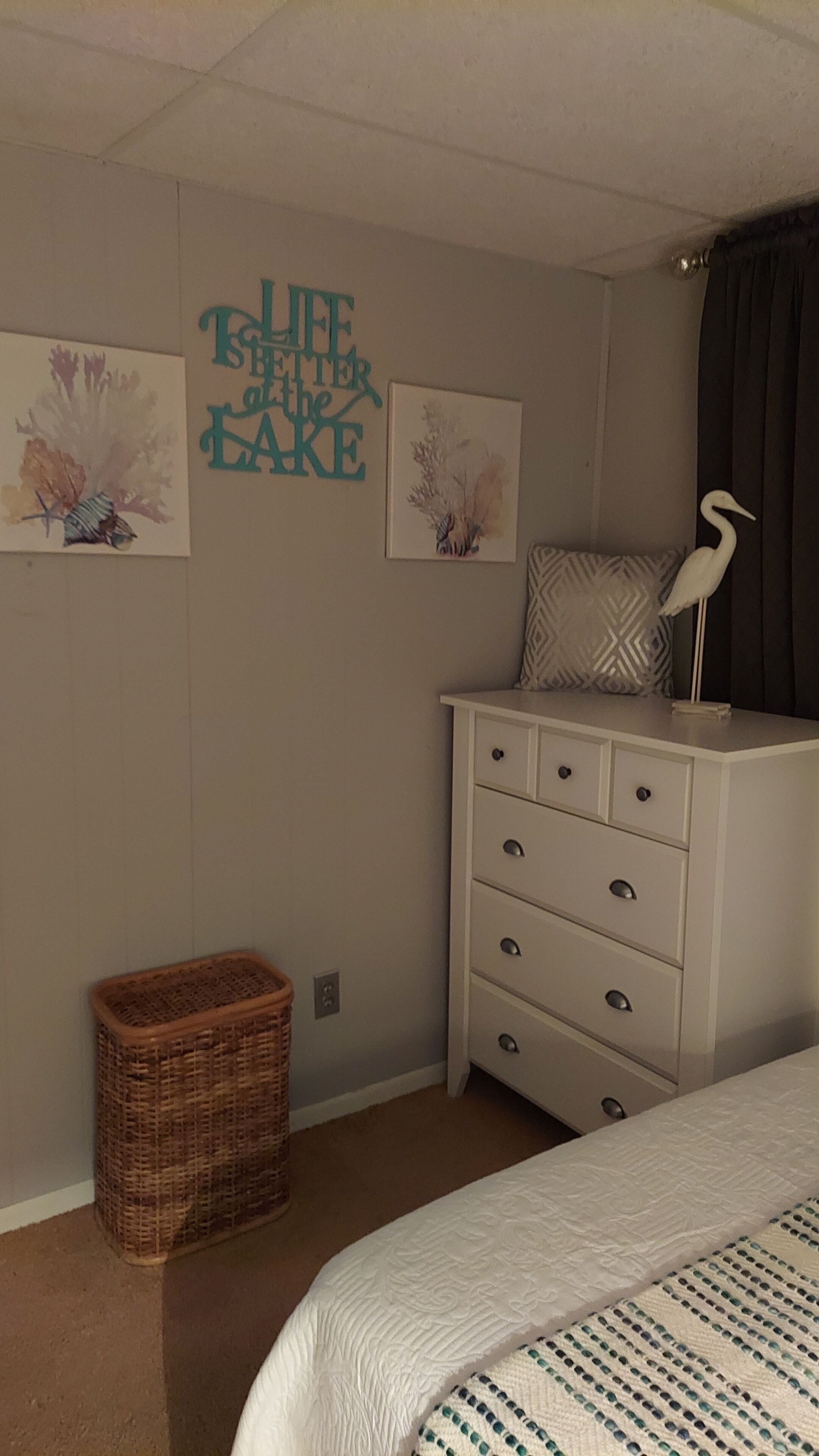A bedroom with a bed, a dresser, a wicker basket, and wall art.