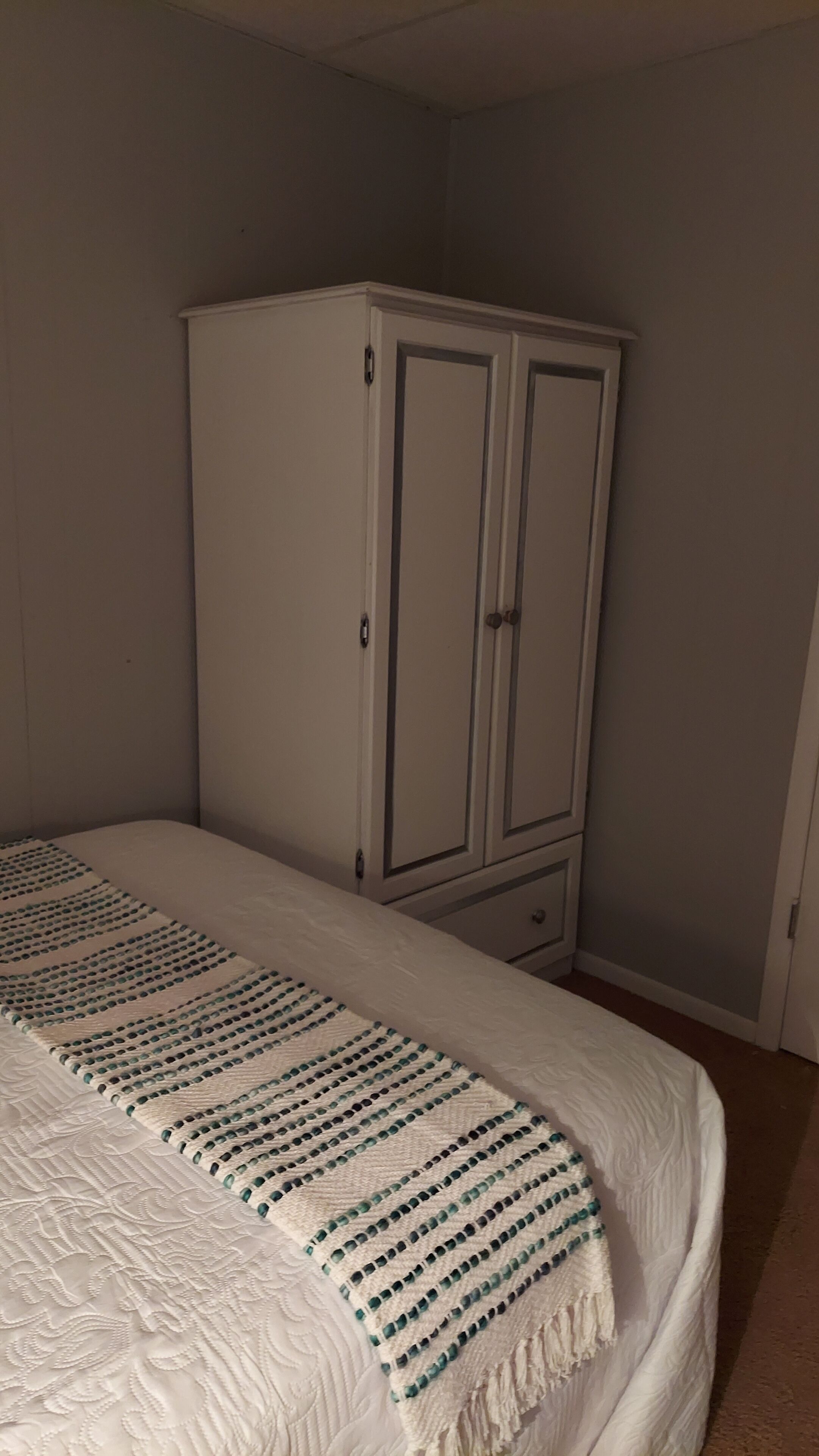 Een slaapkamer met een bed, een witte kast en een deken met dessin.