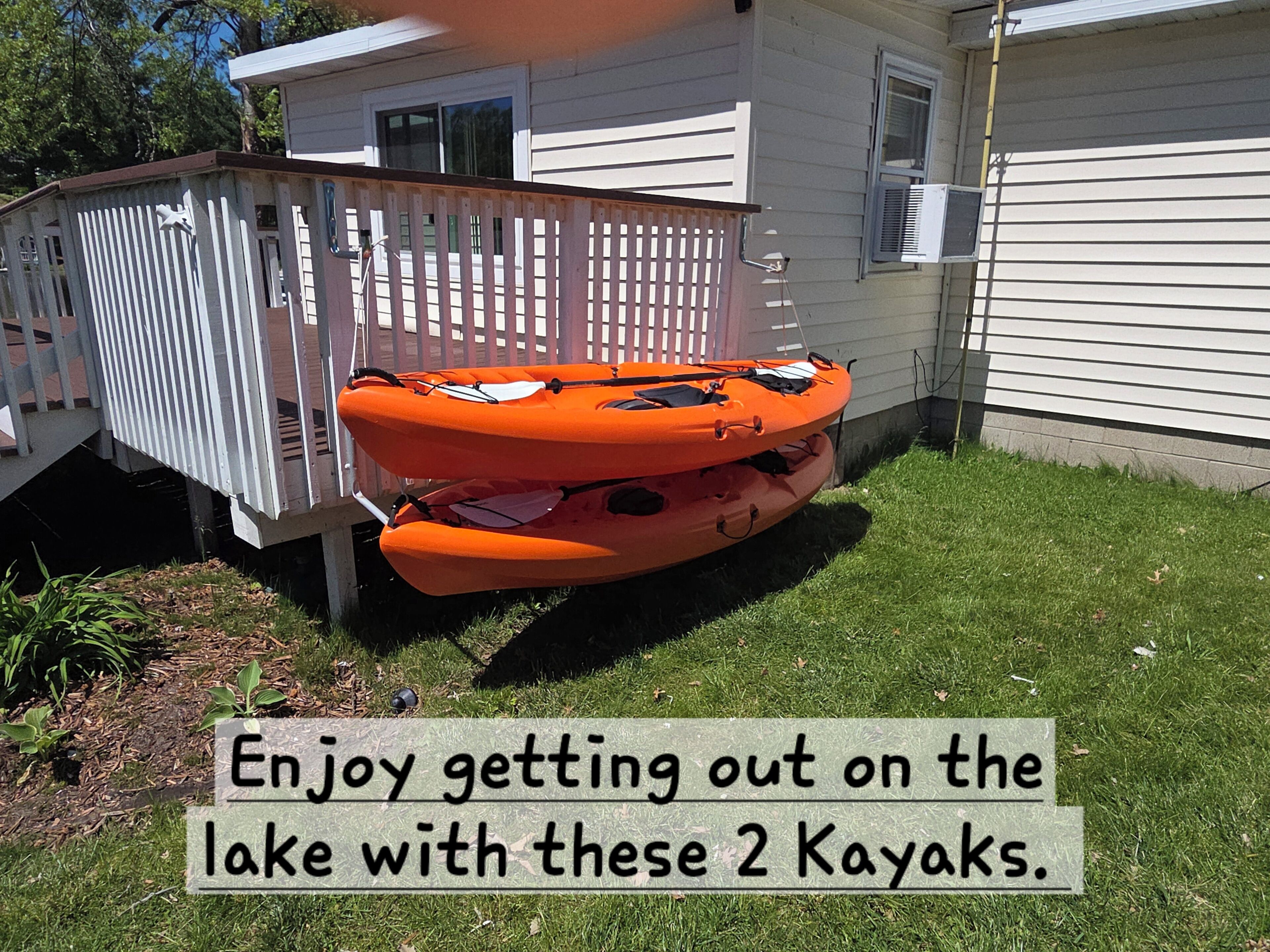 Two kayaks stored in a backyard with a wooden fence and a house in the background.