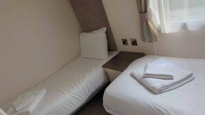 Una habitación pequeña y limpia con dos camas individuales, una mesita de noche y un enchufe en la pared.