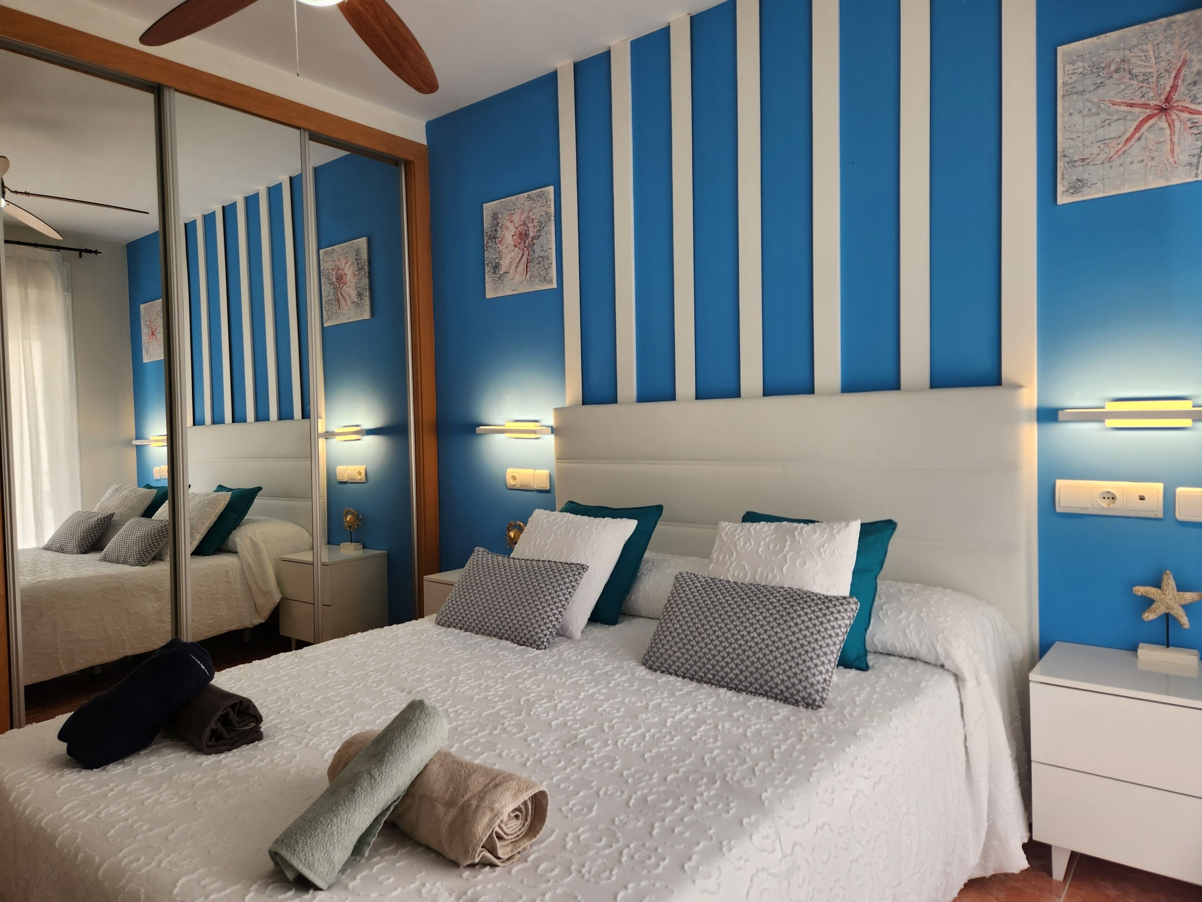 Un dormitori modern amb un llit gran, decoració de paret amb ratlles i un mirall.