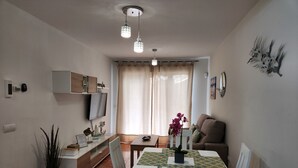 Un coin repas avec une table blanche, des chaises et un téléviseur fixé au mur.