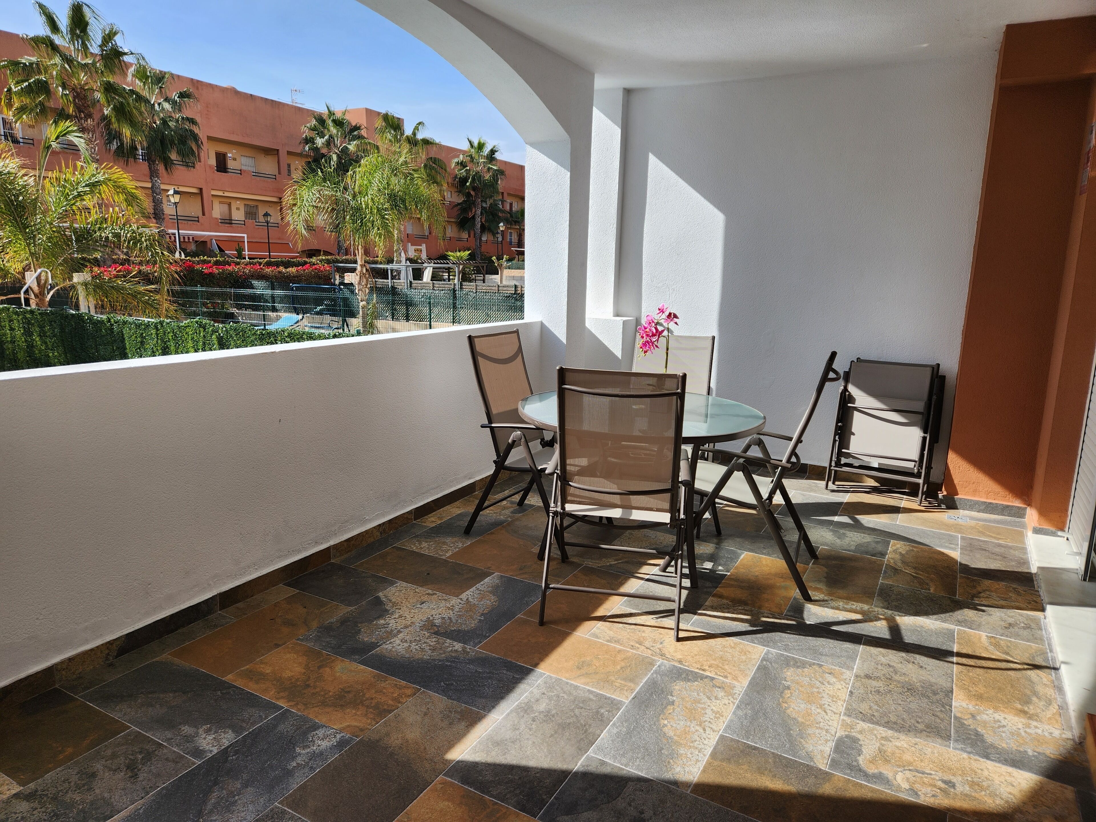 Un balcón con una mesa y sillas, un florero y vistas a una piscina y edificios.