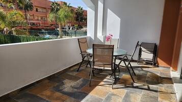 Un balcón con una mesa y sillas, un florero y vistas a una piscina y edificios.