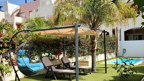 Een tuin met een schommelstoel, een zwembad en een pergola begroeid met planten.