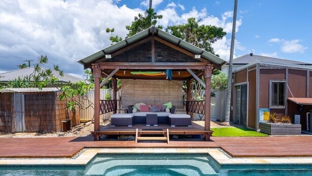 Uma área na piscina com um espaço de estar coberto, um deck de madeira e uma piscina transparente.