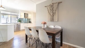 Uma área de refeições com uma mesa de madeira escura, cadeiras brancas e um painel de parede em macramé.