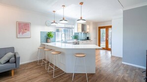 Cozinha moderna com ilha central, banquetas, luminárias pendentes e vista para a sala de jantar.