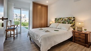 A bedroom with a large bed, wooden headboard, bedside tables, and a view through a glass door. - Silva (Albufeira)