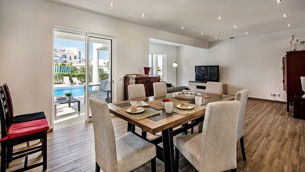 A spacious dining area with a wooden table, multiple chairs, and a television in the background. - Silva (Albufeira)
