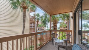A covered balcony with wicker furniture, palm trees, and a view of other buildings.