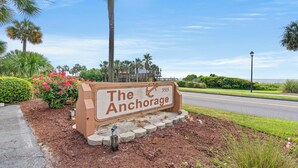 A sign for "The Anchorage" with a beach view in the background.